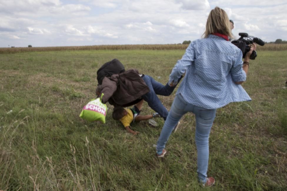 A migrant carrying a child falls after tripping on TV camerawoman (R) Petra Laszlo while trying to escape from a collection point in Roszke village, Hungary, September 8, 2015. Laszlo, a camerawoman for a private television channel in Hungary, was fired after videos of her kicking and tripping up migrants fleeing police, including a man carrying a child, spread in the media and on the internet. REUTERS/Marko Djurica